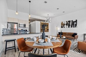 Eine moderne Küche mit eingebauten Geräten, ein Essbereich mit rundem Tisch und Stühlen sowie ein Wohnzimmer mit Sofa und abstrakten Kunstwerken.