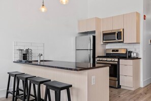 A modern kitchen with a central island, stainless steel appliances, and bar stools. - Lux Stay Near NYC - Patio, Gym & Free Parking (Kearny)