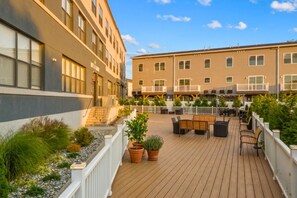 Ein Hotelinnenhof mit Außenbestuhlung, einer Holzterrasse und einem Gebäude mit mehreren Balkonen.