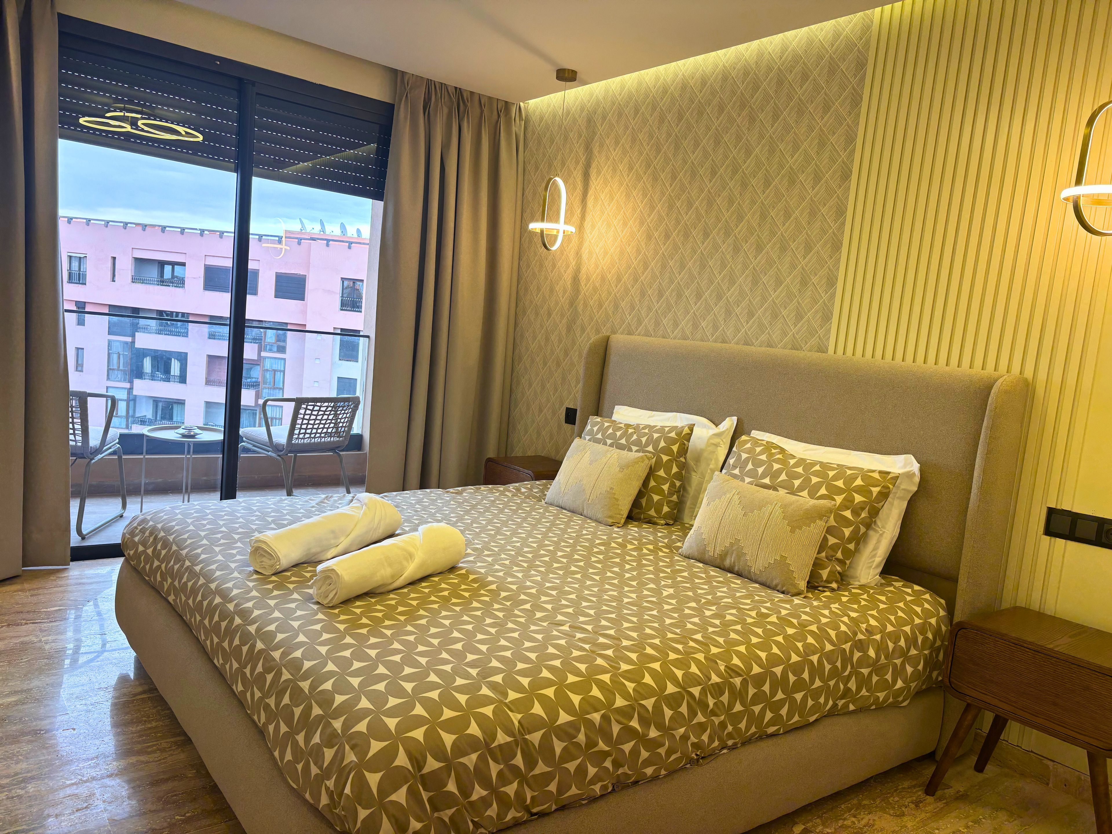 A hotel room with a large bed, a balcony with a chair, and a view of buildings outside.