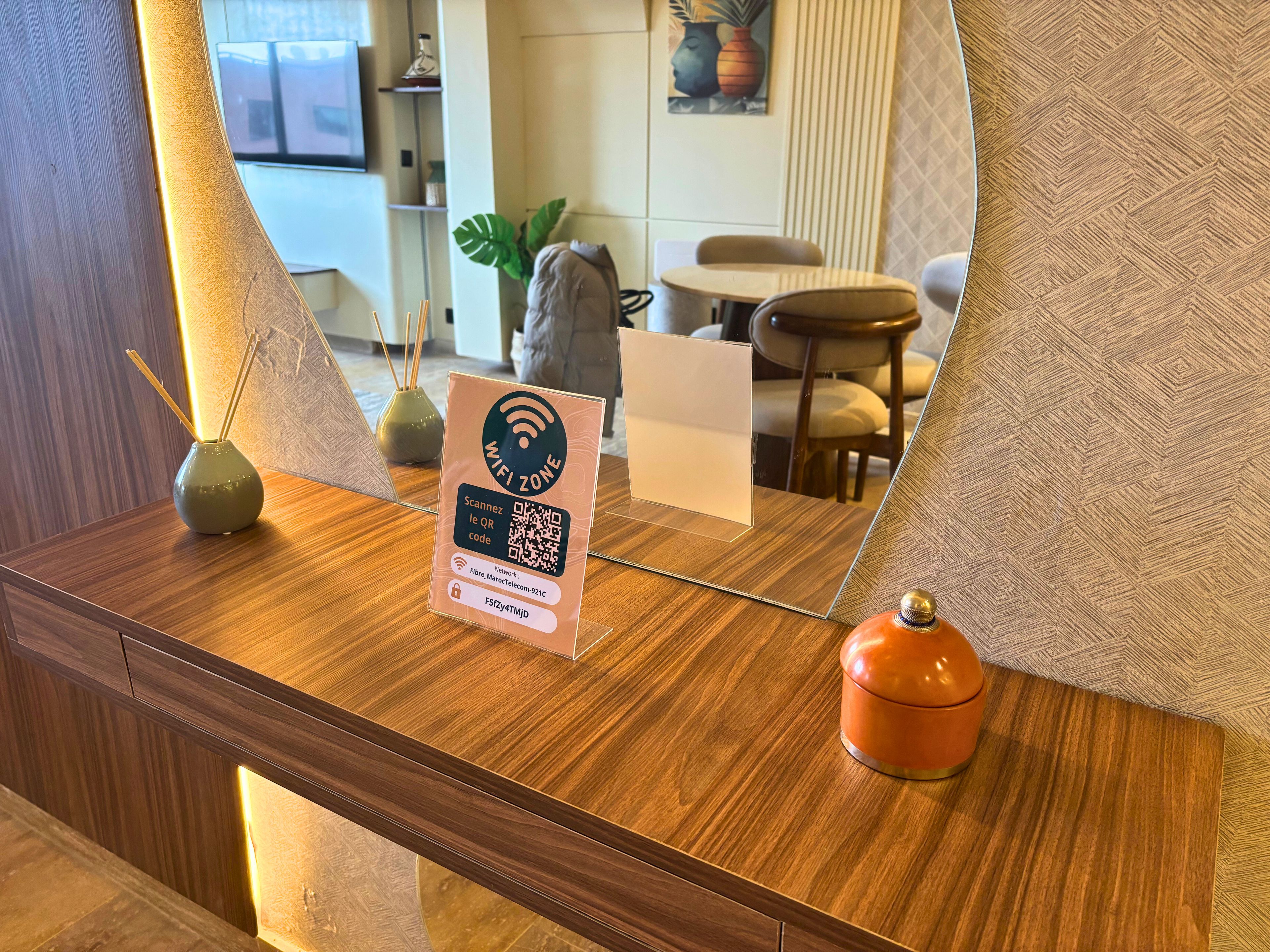 Ein hölzerner Empfangstresen mit einem Schild, das eine WLAN-Zone kennzeichnet, eine Vase mit Schilferdiffusoren und ein kleiner orangefarbener Behälter.