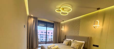 Une chambre d’hôtel moderne avec un grand lit, un balcon offrant une vue sur les immeubles et un éclairage contemporain.