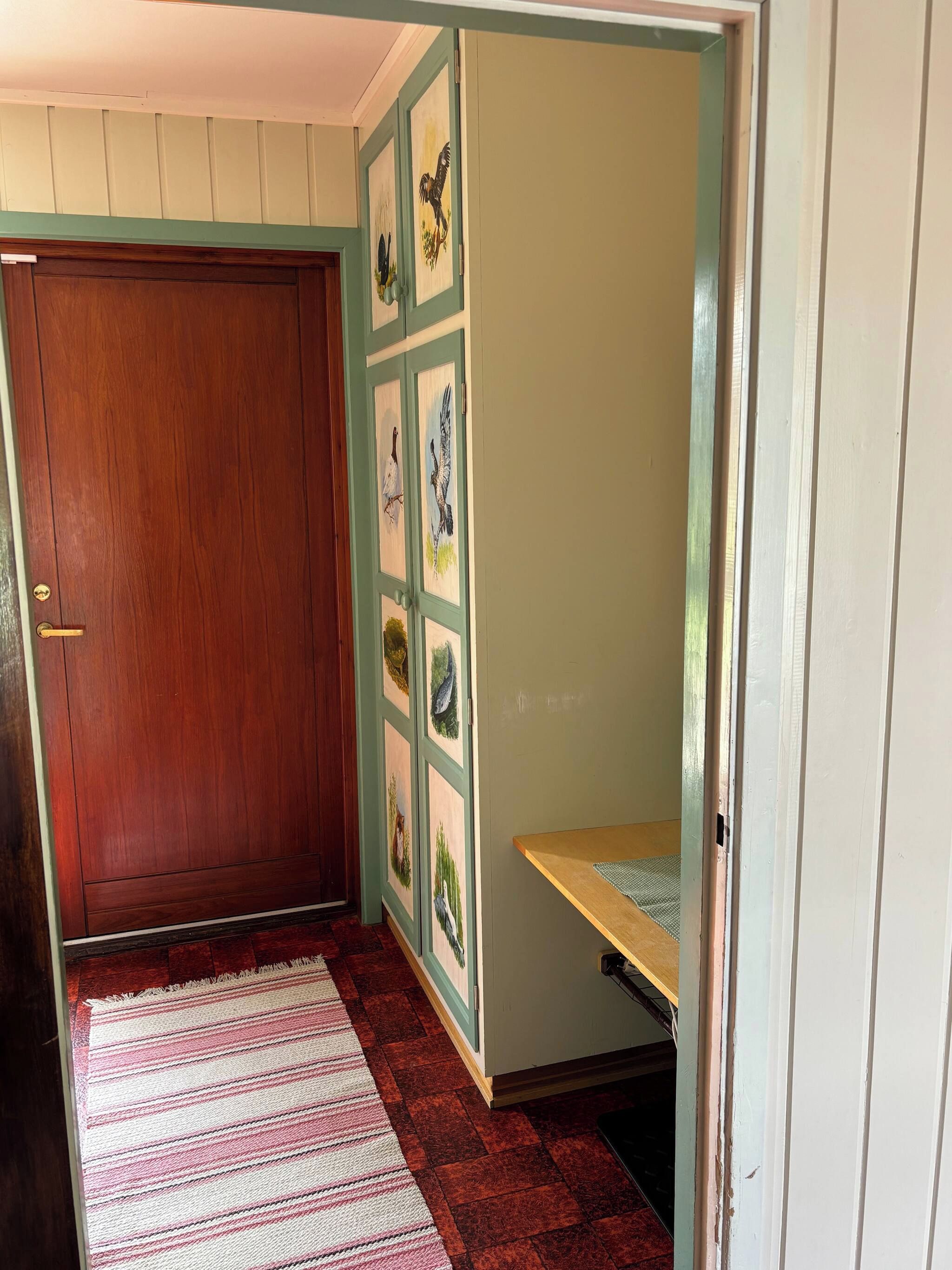 Una habitación con puerta de madera, un banco y una pared con cuadros.