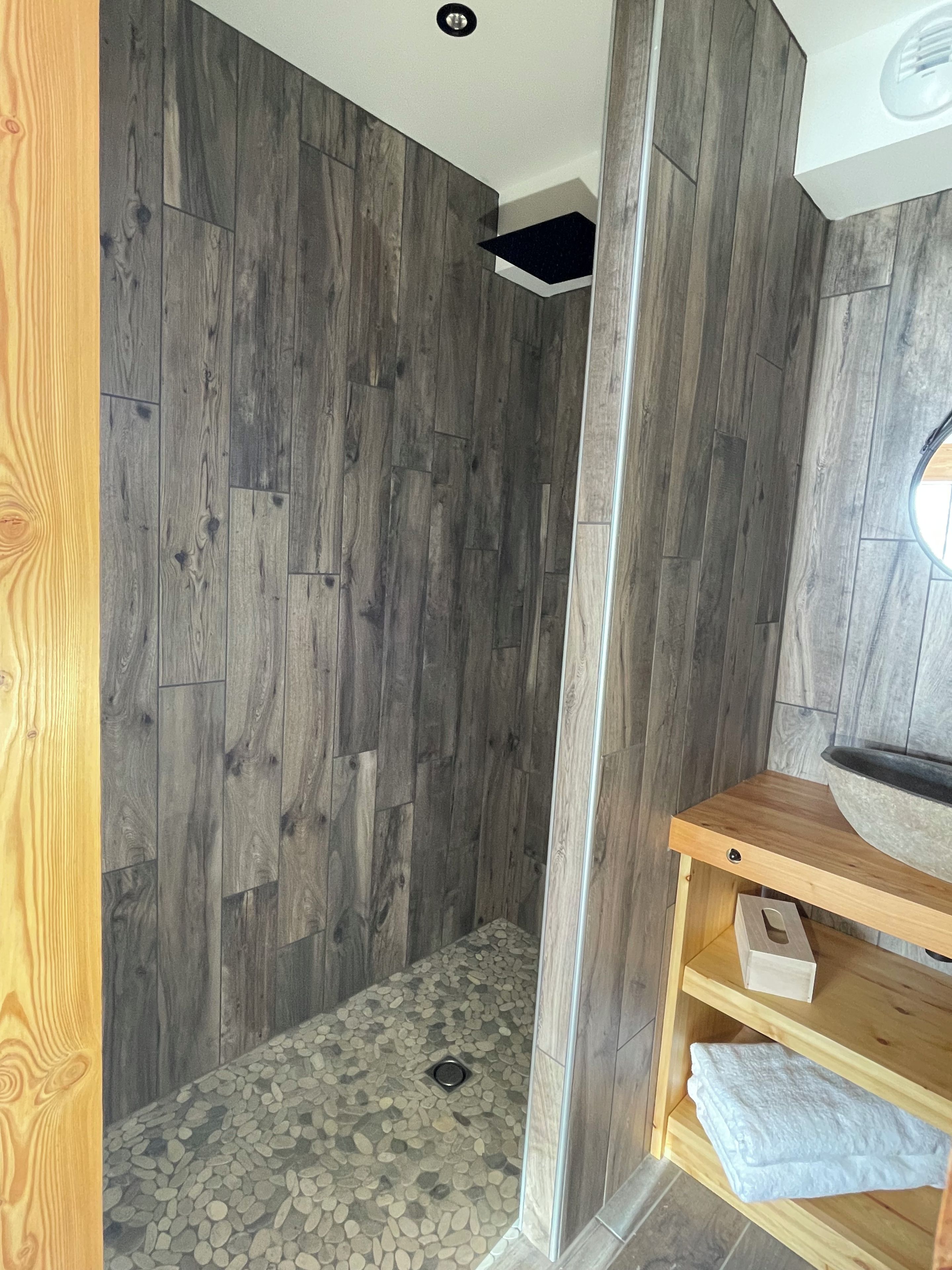 Un angolo doccia con pavimento in legno e fondo della doccia rivestito di ciottoli.