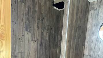 Un angolo doccia con pavimento in legno e fondo della doccia rivestito di ciottoli.
