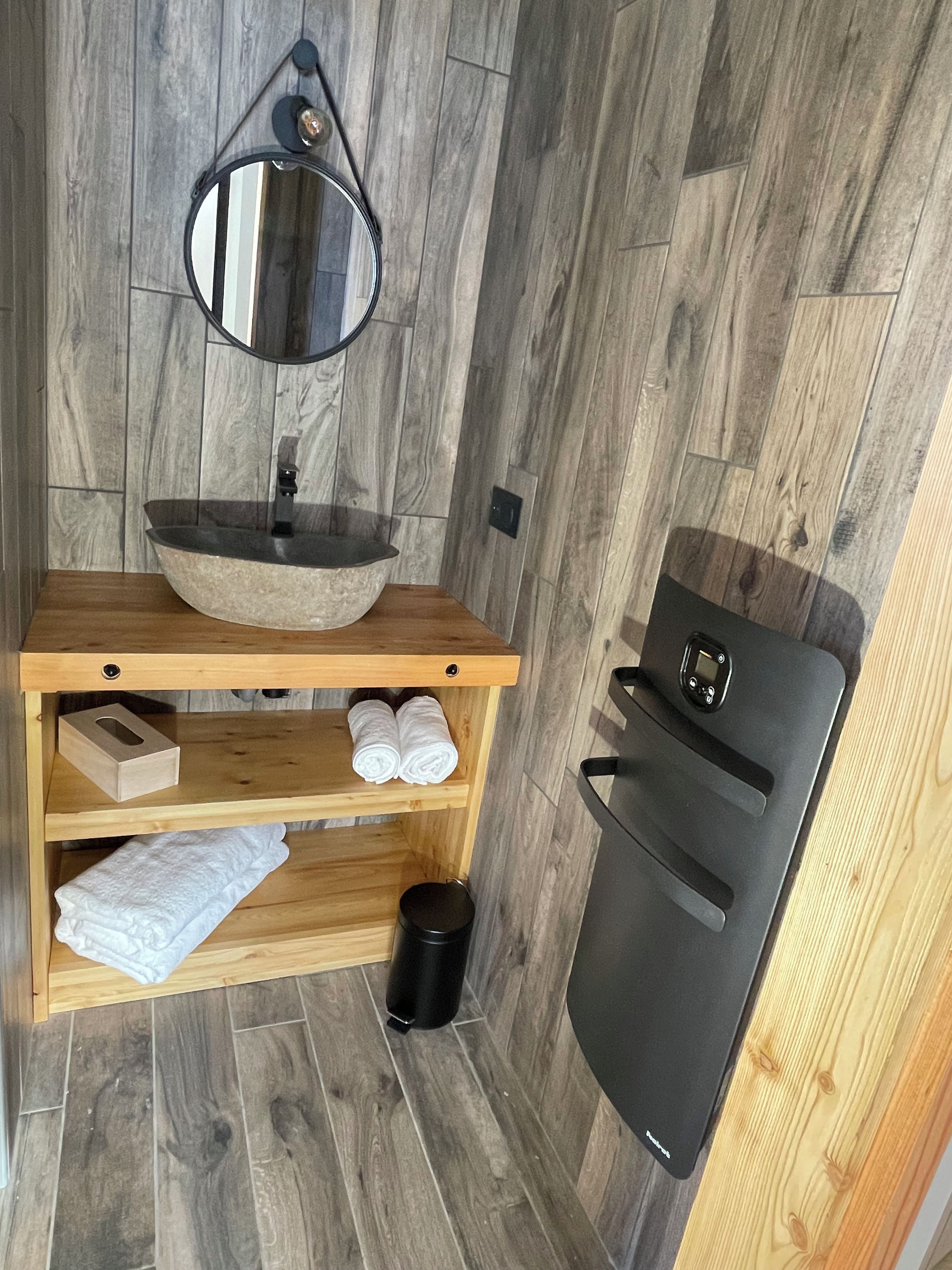 Un bagno con un mobile lavabo in legno, un lavandino rotondo, uno specchio, un portasciugamani e un cestino nero.