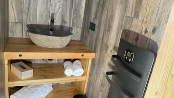 Un bagno con un mobile lavabo in legno, un lavandino rotondo, uno specchio, un portasciugamani e un cestino nero.