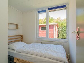 A single bed with a wooden headboard, a window with blue trim, and a view of a red building outside. - Holiday Home in Renesse With Swimming Pool (Renesse)