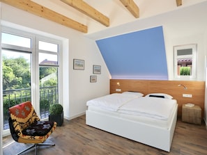 A bedroom with a large bed, a chair with a colorful cushion, a small potted plant, and a window with a view of trees. - Holiday Home in Juist With Swimming Pool (Juist)