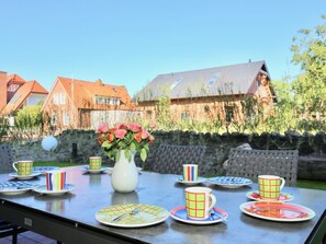 An outdoor dining area with a table set for four, surrounded by a stone wall and houses in the background. - Holiday Home in Juist With Swimming Pool (Juist)