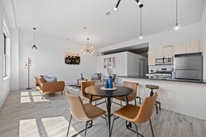 Une cuisine moderne équipée d’appareils électroménagers en acier inoxydable, un coin repas avec une table ronde et des chaises, et un espace de vie comprenant un canapé et une table basse.