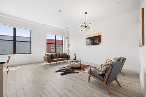 Un vaste espace de vie agrémenté d’une grande fenêtre, d’un canapé moderne, d’une table basse en bois et d’un luminaire au plafond au design original.