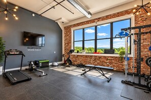 Ein Fitnessraum mit Trainingsgeräten, Laufband und großem Fenster mit Blick auf Grünflächen.