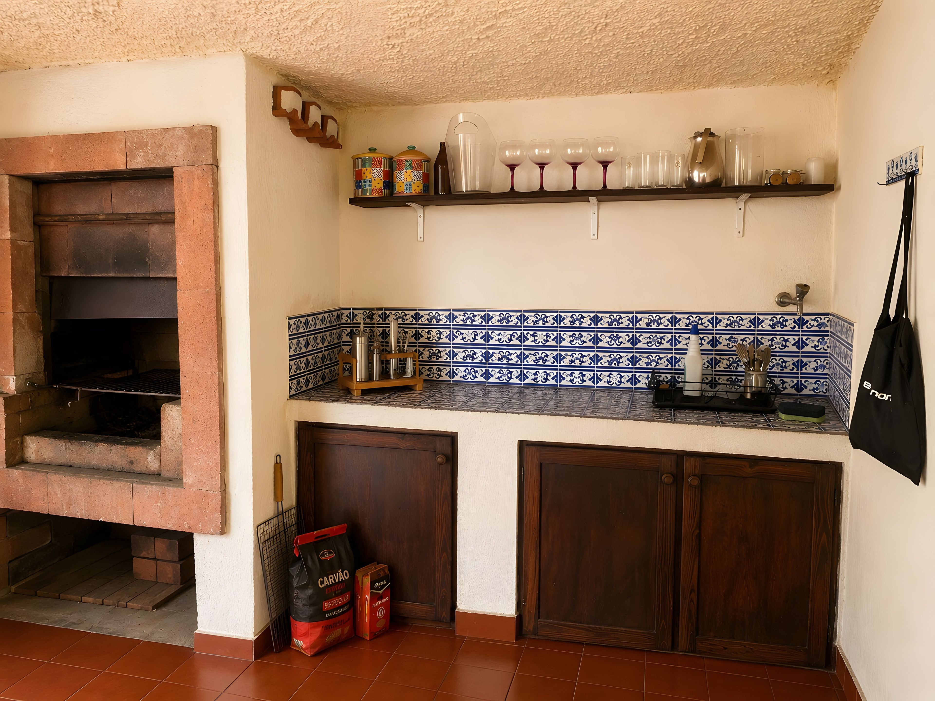 A kitchen with a brick oven, a tiled backsplash, and a shelf with kitchenware.