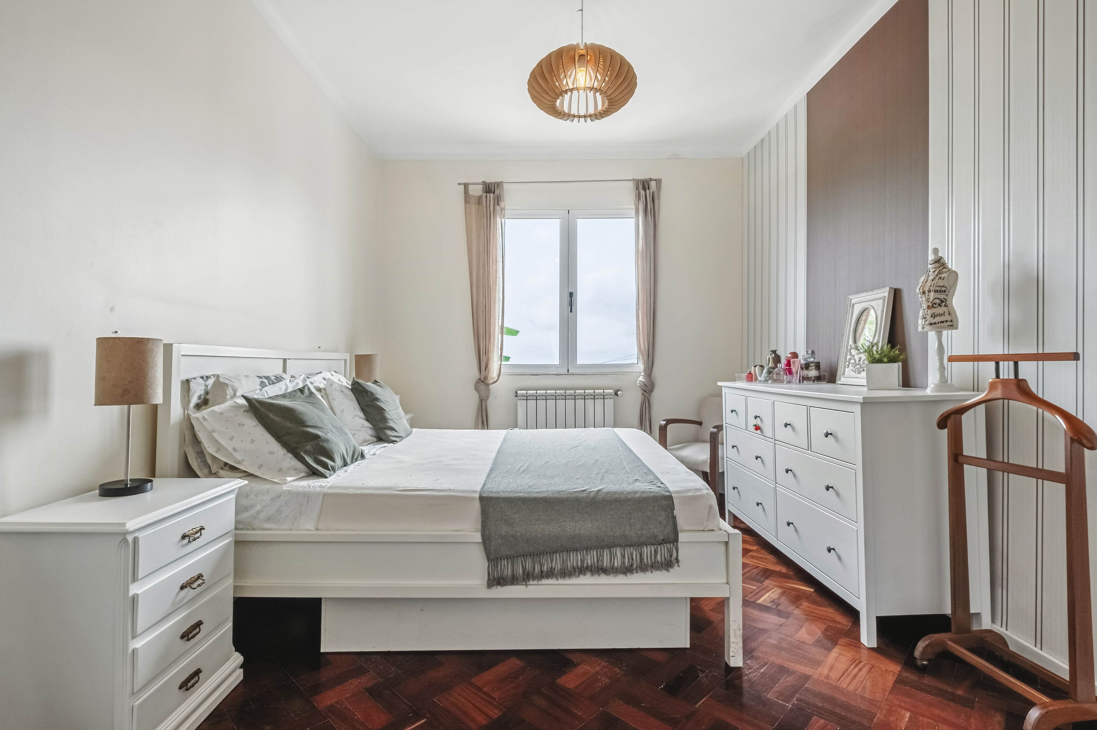 A bedroom with a bed, bedside table, dresser, and a hanging light fixture.