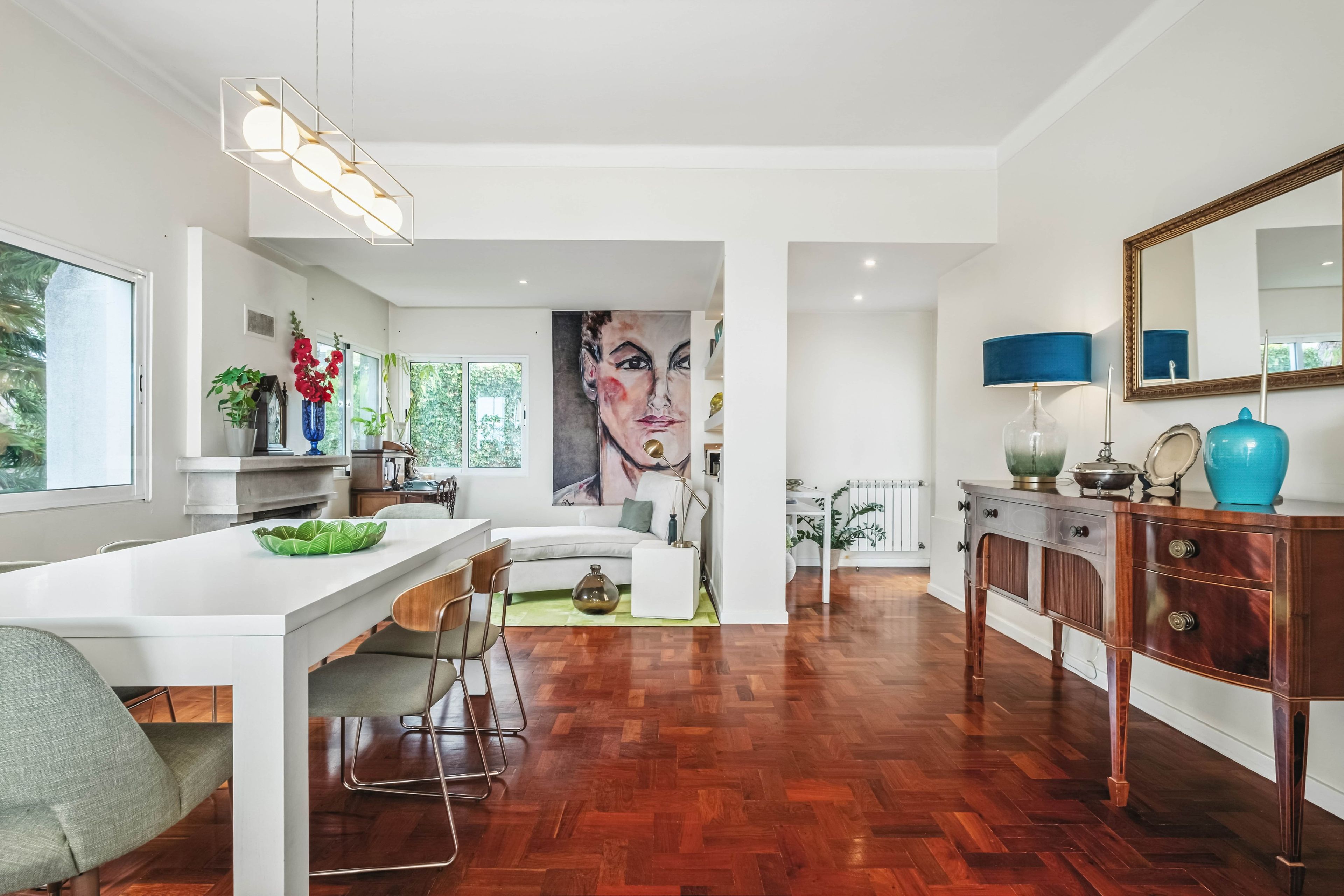A modern interior with a dining area, a large painting, and a wooden floor.