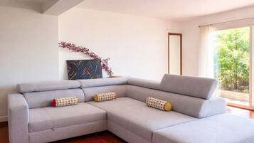 A modern living room with a grey sectional sofa, a red rug, a painting, and a window with a view of greenery.