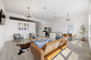 A modern living room with a sofa, a coffee table, and a dining area with chairs. There is a kitchen in the background. - Near NYC High-End Kearny Loft w/ Gym & Patio (Kearny)