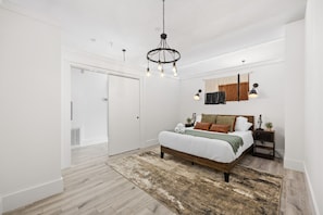 A bedroom with a large bed, a chandelier, a nightstand, and a wall-mounted lamp. - Near NYC High-End Kearny Loft w/ Gym & Patio (Kearny)