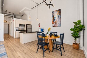 Eine moderne Küche mit Edelstahlgeräten, ein Essbereich mit einem runden Holztisch und schwarzen Stühlen sowie ein großes abstraktes Gemälde an der Wand.