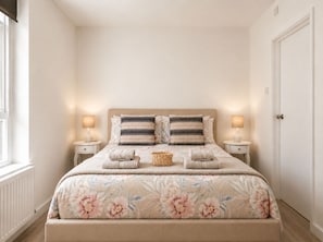 Ein Schlafzimmer mit einem Bett, zwei Nachttischen, einer Kommode, einer Tür und einem Fenster.