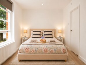Ein ordentlich bezogenes Bett mit Blumenmuster, zwei Nachttische mit Lampen und ein Tablett mit Pflegeprodukten.