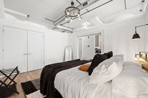A modern bedroom with a bed, a hanging light fixture, and a visible door. - Near NYC, Gym, Patio & Parking - Premium Stay (Kearny)