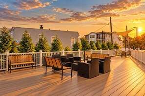 Une terrasse en bois avec des meubles d’extérieur, une clôture blanche et des bâtiments en arrière-plan.