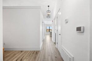 En hall med vita väggar, trägolv, en hängande lampa och en termostat.