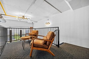 A balcony with two leather chairs and a small table, a ceiling with exposed ductwork, and a wall-mounted light fixture. - Signature Rustic 2BR Near NYC Pets, Gym & Parking (Kearny)