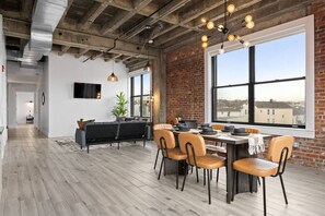 A dining area with a brick wall, large windows, and a modern chandelier. - 20 Mins to NYC Chic Family & Group Loft w/ Gym (Kearny)