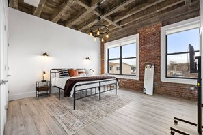 Une chambre avec un grand lit, un plancher en bois, un mur en briques et une fenêtre.