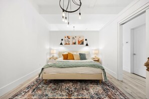 Ein Schlafzimmer mit einem Bett, Nachttischlampen, einem gemusterten Teppich und Wandbildern.