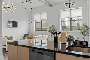 A modern kitchen with a central island, built-in dishwasher, and a coffee bar sign. - 20 Mins to NYC Chic 2BR Loft w/ Gym & BBQ (Kearny)