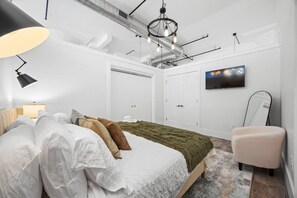 A bedroom with a bed, a chair, a television, and a wardrobe. - 20 Mins to NYC Chic 2BR Loft w/ Gym & BBQ (Kearny)