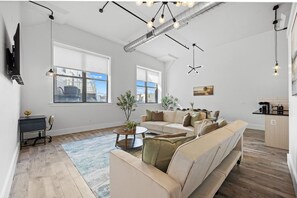 A modern living room with a sofa, a coffee table, and a TV on the wall. - 20 Mins to NYC Chic 2BR Loft w/ Gym & BBQ (Kearny)