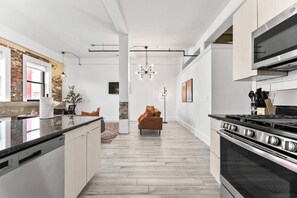 A modern kitchen with a central island, a dining area with a sofa, and a large stove. - NYC 20 Min Designer Loft | Gym, Desk & Parking (Kearny)