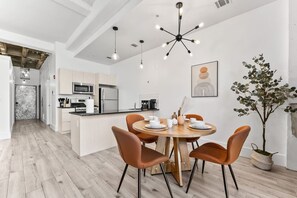 A modern kitchen with white cabinets, a central island, and a dining area with a round table and chairs. - NYC 20 Min Designer Loft | Gym, Desk & Parking (Kearny)