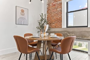 A dining area with a round wooden table, four brown chairs, and a vase with pampas grass. - NYC 20 Min Designer Loft | Gym, Desk & Parking (Kearny)