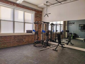 A gym with weightlifting equipment, a large mirror, and a brick wall. - NYC 20 Min Designer Loft | Gym, Desk & Parking (Kearny)