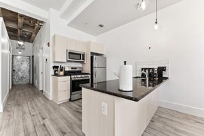 A modern kitchen with a central island, stainless steel appliances, and a wooden floor. - NYC 20 Min Designer Loft | Gym, Desk & Parking (Kearny)