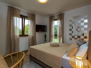 Ein Schlafzimmer mit einem Bett, einem Fernseher, einem Wandspiegel und einem Fenster mit Vorhängen.