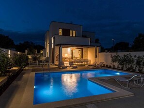 Ein modernes, zweistöckiges Haus mit Außenpool, Essbereich und Außenmöbeln sowie einer gut beleuchteten Eingangspartei.