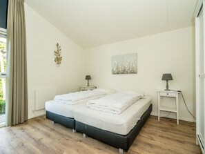 A double bed with white linens, two bedside tables with lamps, a wall art piece, and a window with curtains. - Holiday Home in Renesse With Swimming Pool (Renesse)