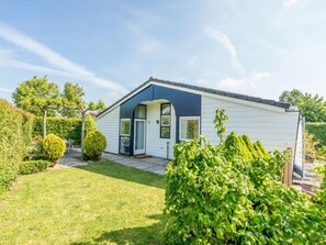 A single-story house with a dark blue front door, a small porch, and a well-maintained garden with a hedge and a trimmed bush. - Holiday Home in Renesse With Swimming Pool (Renesse)