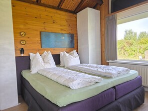 A double bed with a green and purple mattress, a wooden headboard, and a view of greenery outside. - Holiday Home in Zoutelande With Barbecue (Zoutelande)