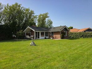 A single-story house with a covered porch, a lawn, and a hedge. - Holiday Home in Zoutelande With Barbecue (Zoutelande)