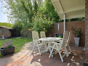 An outdoor patio with a round table and four chairs, surrounded by a brick wall and greenery. - Holiday Home in Zoutelande With Barbecue (Zoutelande)