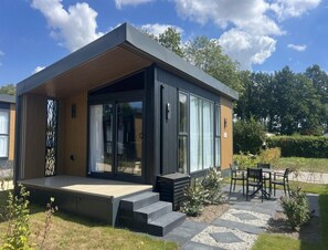 A modern house with a flat roof, large windows, and a patio with outdoor furniture. - Romantic Coastal Chalet for 2 (Scherpenisse)