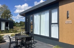 A modern building with large windows, a patio with outdoor furniture, and a sign indicating room number S-POD 4. - Romantic Coastal Chalet for 2 (Scherpenisse)